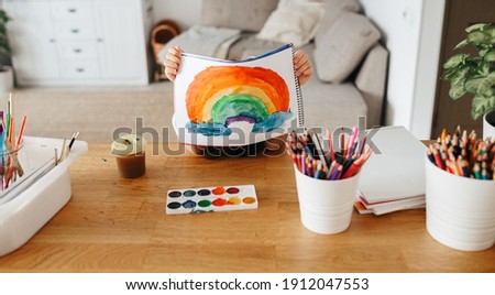 Kids painting watercolor rainbows at table at home. Arts and crafts