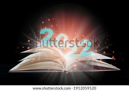 New year 2022 on open white paper fantasy book with shining pages isolated on black background. Miracle happiness holiday concept and mystery beginning idea