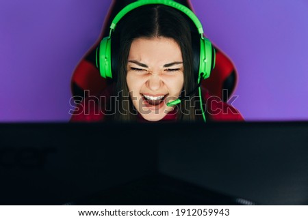 The gamer sits on a gaming chair and plays computer games. The player has green headphones on his head.