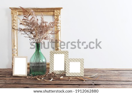 frame and dried flowers in green vase on old wooden shelf