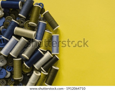 Layout of yarn on spool and sewing buttons on yellow background, copy space for text. Trendy color 2021. Sewing, tailor tools and  hobby pattern. Background or templates of crafts and dress making. 