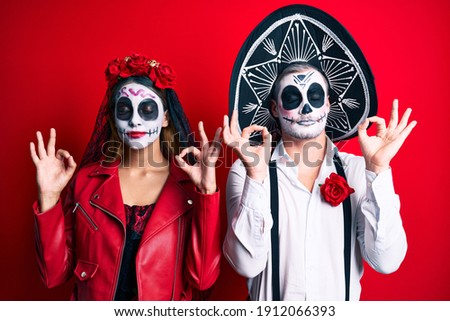 Couple wearing day of the dead costume over red relax and smiling with eyes closed doing meditation gesture with fingers. yoga concept. 