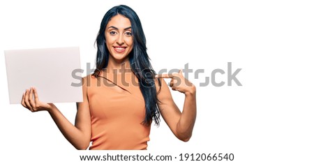 Beautiful hispanic woman holding blank empty banner pointing finger to one self smiling happy and proud 