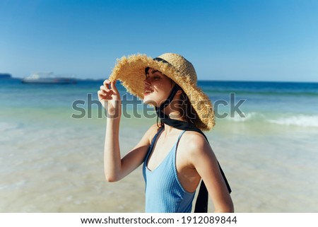 slender woman in a blue swimsuit and hat near the sea on the beach