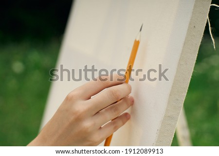 pencil in a female hand and easel on nature landscape artist
