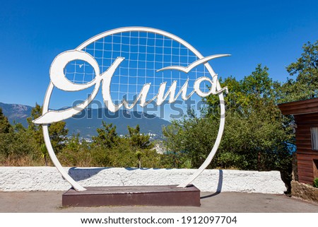 Yalta. The inscription in Russian in white “Yalta” on a metal stele in the shape of a circle in good summer weather.