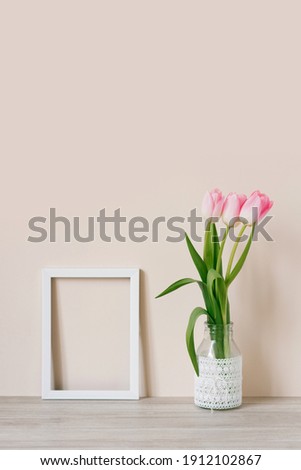 Home interior with decor elements. Mockup with a white frame and pink tulips in a vase on a light beige background