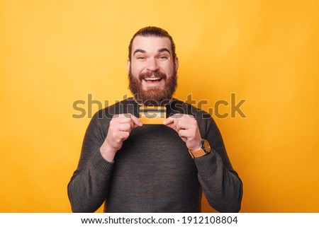 Photo of happy man with beard holding credit card over yellow background.