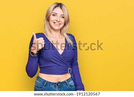 Young caucasian woman wearing casual clothes doing happy thumbs up gesture with hand. approving expression looking at the camera showing success. 