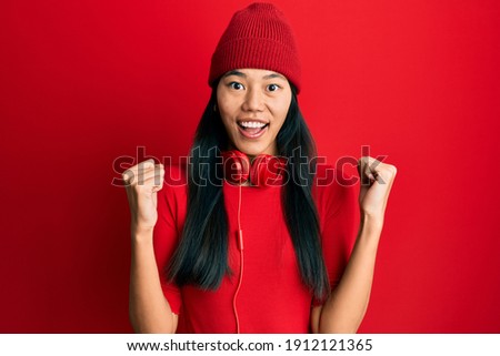 Young chinese woman listening to music using headphones celebrating surprised and amazed for success with arms raised and open eyes. winner concept. 