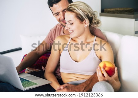 Healthy lifestyle young couple at home enjoy technology and natural food together working on laptop computer and eating an apple - people in rhappy elationship during lockdown coronavirus