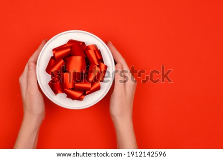 Female hands holding a festive box with ribbons and bows. Red festive background top horizontal view copyspace.