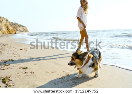Candid lifestyle image happy woman with her pet Corgi dog having fun together at seashore of summer beach in morning