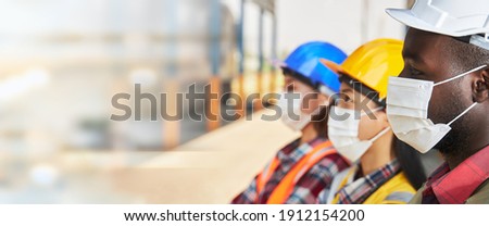 Portrait of industrial workers wearing surgical masks, standing on top of together in layers within the factory.