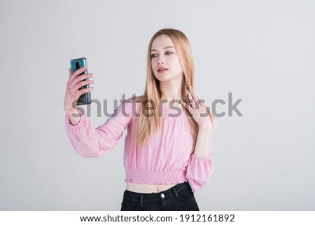 Portrait of a blonde girl who takes a selfie in the studio on a white background