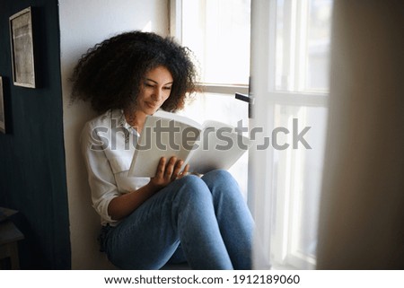 Portrait of young woman with book indoors at home, reading. Royalty-Free Stock Photo #1912189060