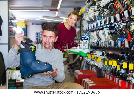 Woman assistant is helping man to trying on ski boots in store.