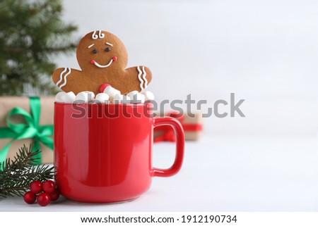 Gingerbread man in red cup with marshmallows on white table, space for text