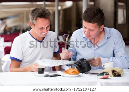 two cheerful men sitting with coffee and looking at map at a table in cafe