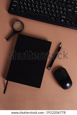 Workplace with keyboard,mouse wireless, black notebook and pen on a brown background. Copy space
