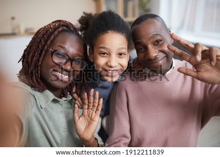 POV shot of happy African-American family smiling at camera while taking selfie-photo at home or using video chat