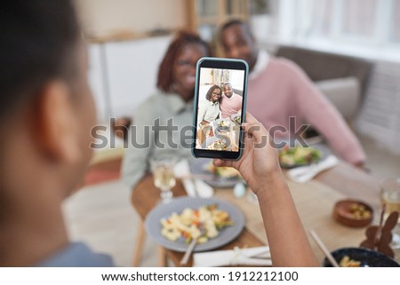 Close up of African-American girl taking photo of parents at dinner table in home interior, focus on smartphone screen, copy space