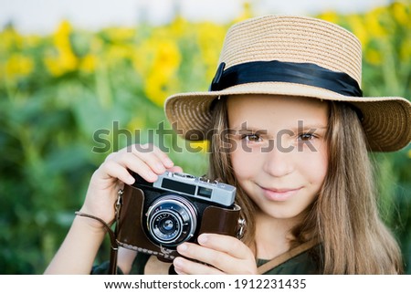 A girl in a straw hat holds a film camera with her hands, looks into the lens and smiles