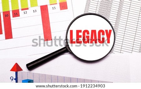 On the desktop, graphs, reports, a magnifying glass with the inscription LEGACY. Business concept