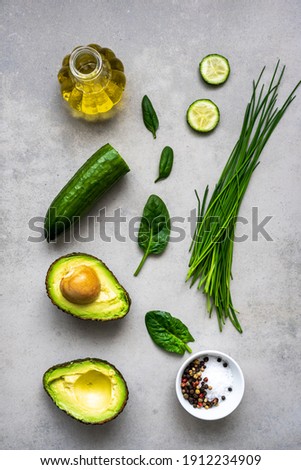 Green vegetables and a halved avocado, salt and peppercorns in a bowl and cooking oil on a gray background. Flat lay, healthy eating, in a row. 