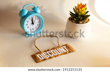 The text of Discounts is written on a paper tag lying on a white background, next to a cactus flower and a cactus flower.