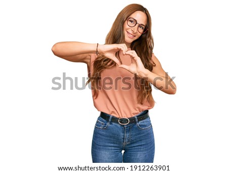 Young hispanic woman wearing casual clothes and glasses smiling in love doing heart symbol shape with hands. romantic concept. 