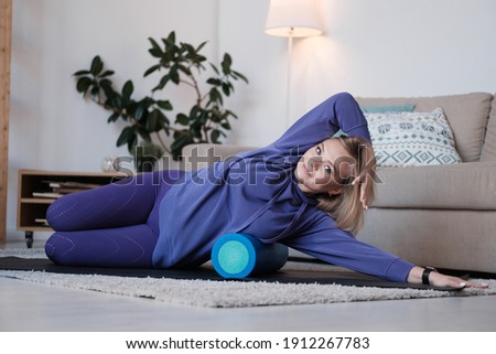 Staying fit and healthy. Beautiful young woman in sports clothing doing yoga with a roller at home