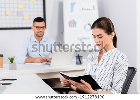businesswoman looking at notebook near businessman on blurred background