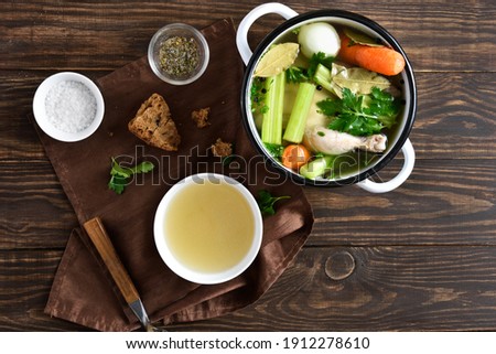 Chicken broth with vegetables and spices on wooden background. Top view, flat lay