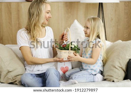 Happy mother day. Child daughter congratulates mom and gives her basket of spring flowers and postcard with heart drawing. Family and childhood concepts