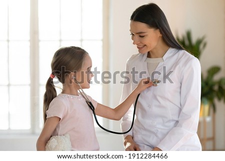 Cute small girl child hold stethoscope listen to female nurse heart at consultation in hospital. Caring woman doctor have fun play with little kid patient in clinic. Children healthcare concept. Royalty-Free Stock Photo #1912284466