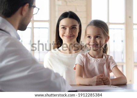 Happy young Caucasian mom and little 7s daughter have consultation with male doctor in private clinic. Smiling mother and small girl child talk speak with man GP or pediatrician. Childcare concept. Royalty-Free Stock Photo #1912285384