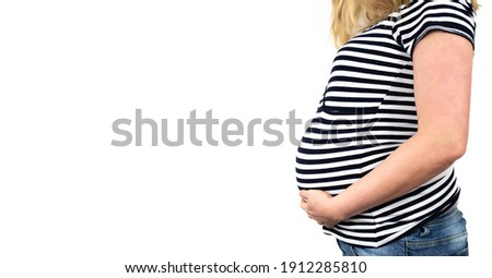 side view of midsection of 9 months pregnant woman in striped top an jeans with hands on belly against white background