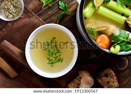 Chicken broth with vegetables and spices on wooden background. Top view, flat lay