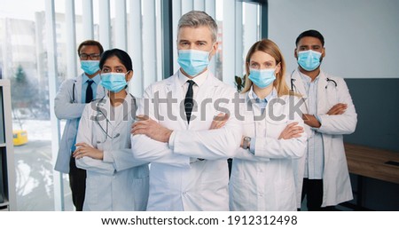 Portrait of serious experienced different mixed-races healthcare workers doctors and physicians in medical masks posing in clinic looking at camera, quarantine concept, team colleagues Royalty-Free Stock Photo #1912312498