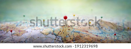 Pins on geographic map curved like mountains. Pinning a location on map with mountains. Adventure, discovery, navigation, geography, mountaineering, rock climbing, hike  and travel concept background Royalty-Free Stock Photo #1912319698