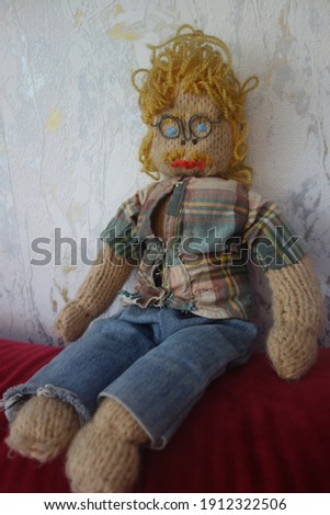 Knitted and crocheted male doll in the shape of a blond man with a mustache, curly hair, glasses, jeans and checked shirt. Handcrafted from upcycling material. Stereotypical geek nerd engineer figure.
