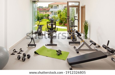 Modern concept of green nature eco style gym. Front view of stylish training room interior in hotel, apartment, house with open air garden window Royalty-Free Stock Photo #1912326805