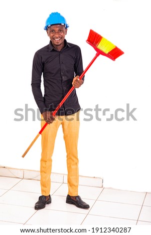 portrait of a young male construction engineer holding a broom while smiling.