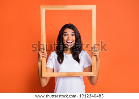 Portrait of impressed girl wear white t-shirt hold frame isolated on orange color background