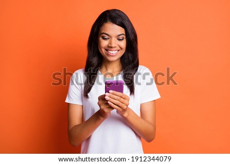 Photo of optimistic girl hold telephone wear white t-shirt isolated on orange color background