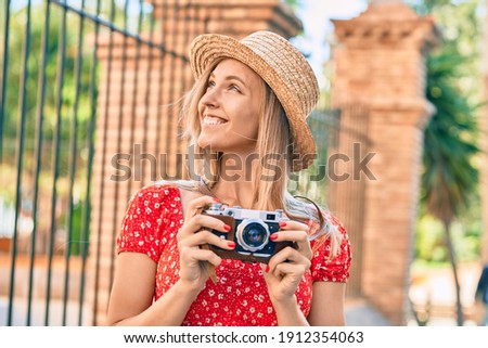 Young blonde tourist woman wearing summer style using vintage camera at the city.