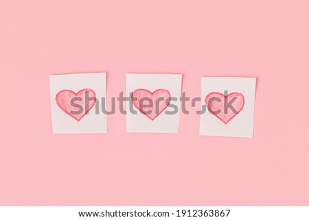 Three hearts drawn in pencil on pieces of white paper on a pink background.