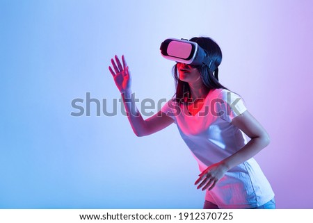 3D simulation, have fun, testing new device, digital technology and modern entertainment. Cheerful young asian lady in virtual reality glasses plays in online game, in neon, studio shot, free space