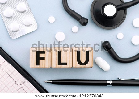 Word FLU on wooden cubes on blue background with stethoscope, pills, capsules, pen and cardiogram. Medical concept. Flat lay, top view.